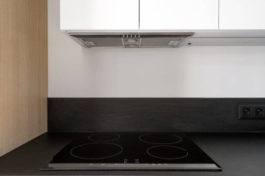 Modern ev aletleri. Siyah tezgahta cam seramik soba ve modern iç mimarisi olan şık mutfakta sökücü kaputu. Kontrol paneli ile boş indüksiyon hob