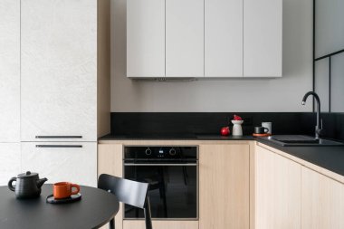 Modern mutfak tasarımı minimalist tarzda yuvarlak masa, parlak renkli ahşap mobilyalar ve entegre ekipmanlar. Seramik sofra takımı siyah lavabonun yanında.