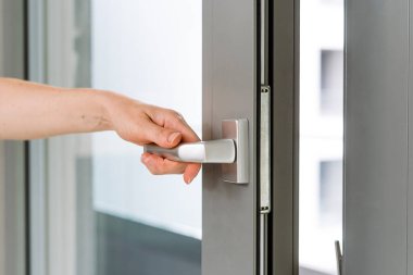 Kadın eli gümüş tutacağı ve içerideki havalandırma için plastik pvc penceresi açık. Balkon kapısını kapatan kişiye yakın çekim.