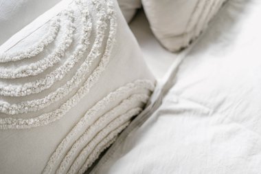 Yatak odasındaki rahat yatakta yastıkta dekoratif elementlerin olduğu keten bej yastık kılıfına özen göster. Ev için tekstil. Doğal malzemelerden yatak..