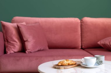 Kahve masasının mermer tezgahına ve modern oturma odasındaki kırmızı rahat kanepeye karşı kruvasanla ahşap tahtaya odaklan. Evde kahvaltı..