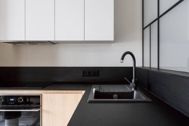 Yeni mutfakta modern iç mekan, siyah tezgahta musluğu olan granit lavabo, cam seramik indüksiyon sobası, elektrikli fırın ve dolap. Moda apartmanında entegre ev aletleri