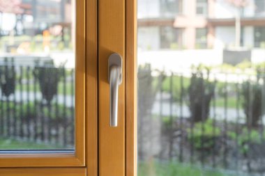 Ahşap pencere çerçevesinde tut. Kapalı balkon kapısı, şeffaf camlar, binalar ve bulanık arka planda yeşillik. Yüksek kaliteli metal-plastik profiller ve odada gürültü azaltma kavramı