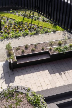 Yüksek açılı çatı bahçesi, siyah metal bir bank ve taş bir patika. Şehirde rahat yaşamak için modern peyzaj tasarımı