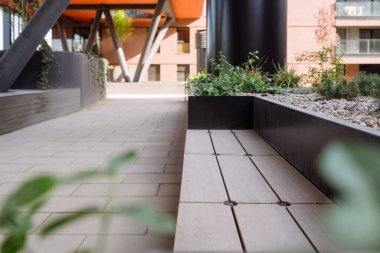 Beton bir yol, yeşillik ve ahşap bir bankla dolu modern bir avluya çıkar..