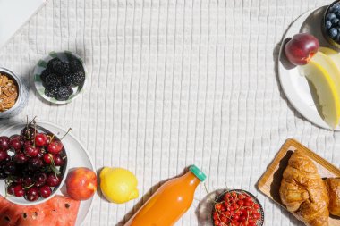 Beyaz piknik battaniyesine çeşitli meyveler, hamur işleri, böğürtlen ve meyve suyu ile yer kopyala. Karpuz, kavun ya da kavun, kırmızı kiraz, böğürtlen, limon ve şeftali.