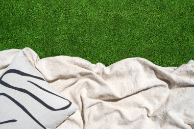 Beyaz ekose ve dekoratif yastıklardan oluşan düz bir yatak yeşil çimenlerin üzerinde uzanıyor. Bahçede piknik battaniyesi, üst manzara. Bahçede dinlenme ya da yazın park kavramları