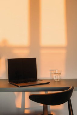 Uzak iş, yaratıcı endüstri, ilham blogu konsepti. Günbatımı ışığı ve minimalist tarzda modern bir dairede masa, dizüstü bilgisayar ve sandalye ile rahat bir iş yeri. Detaylar iç kısımda