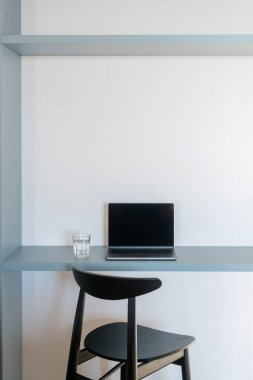 Kablosuz teknoloji, internet bağlantısı, iletişim kavramları. Ofisteki mavi minimalist masada boş ekranlı kişisel dizüstü bilgisayar. Ahşap sandalye ve modern mobilyalar.