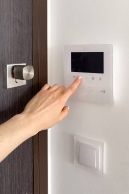 Evde dahili telefon kullanan bir kadın. Kadın cevap veriyor, düğmeye basıyor ve apartmanın ön kapısını açıyor. Modern apartman gözetleme ve güvenlik sistemi, dikey çekim