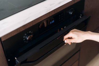Modern mutfak. Kadın elinin yüksek açılı görüntüsü fırını açar ve fırında pişmiş hamur işi, ekmek veya yiyeceğin hazır olup olmadığını kontrol eder. Evde elektrikli ev aletleriyle yemek pişirme kavramı