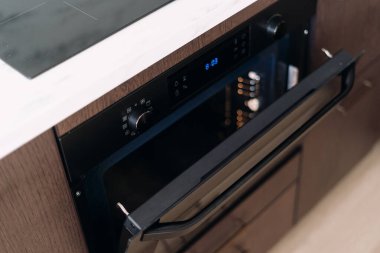 Yeni elektrikli fırının yüksek açılı görüntüsü açık kapı ve mikrodalga fırın altında ahşap mutfak dolabında inşa edilmiş. Ev aletleri kavramı, modern iç mimarisi olan bir daire.