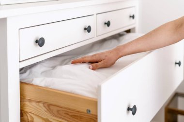 Beyaz çekmecelerden klasik tarzda yorgan çeken bir kadın, yaklaşın. Yatak odasının içi eski mobilyalarla dolu. Depo için şık bir tuvalet. Taze yatak ve tekstil.