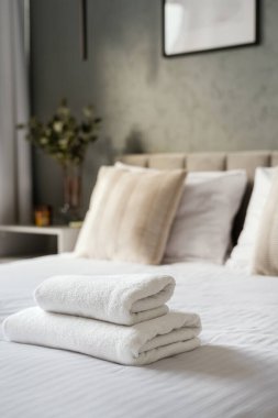 Beyaz bir battaniye ve üzerinde iki katlanmış havluyla düzgünce yapılmış bir yatak. Sabah duşu için banyo tekstili olan misafir yatak odası kavramları. Misafirperverlik ve oda servisi, dikey çekim