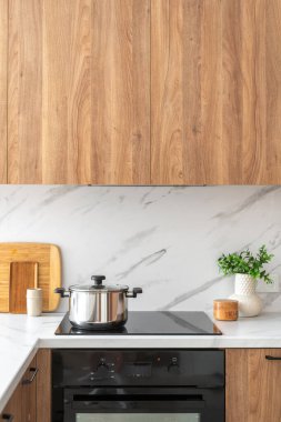 Modern mutfakta ahşap dolaplar. Siyah bir sobanın üstündeki paslanmaz çelik tencerenin dikey görüntüsü. İç tasarım, evde yemek pişirmek için ev aletleri.