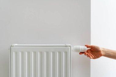 Radyatörün termostatını ayarlayan kişi odada rahat bir sıcaklık yaratıyor. Modern binalardaki merkezi ısıtma sistemi. Doğal kaynakların tüketimi, enerji tasarrufu ve ısı eksikliği kavramı