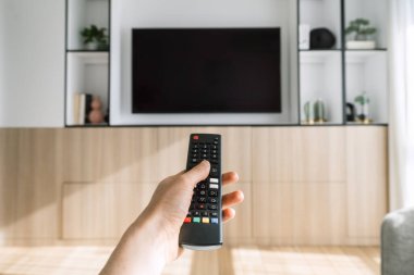 Bir el, ahşap bir eğlence merkezine monte edilmiş düz ekran televizyonun önünde uzaktan kumandayı tutuyor. Kadın düğmesine basar, kanalı değiştirir, evde film izleriz. Uzayı kopyala, maketle