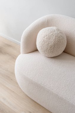 Oturma odasının iç tarafındaki beyaz koltuğun üzerinde yüksek açılı pelüş yastık manzarası. Yuvarlak yastıklı minimalist kanepe. Ahşap zemin ve yumuşak döşeme mobilyaları. Kuru temizleme konsepti, dikey çekim