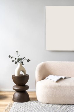 Beyaz duvardaki şablon çizimi. Üzerinde dergi olan rahat bir kanepe halıya oturur. Koltuğuna yakın beyaz vazosu ve yeşilliği olan küçük bir masa. Oturma odasındaki soyut resmin altındaki kanepe.