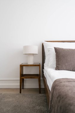 Rahat yatağı, yastığı, dekoratif yastığı ve okuma lambasıyla komodinin yanındaki battaniyesi olan beyaz bir otel odası. Modern dairede yatak odası mobilyası. Evde sabahlar