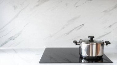 Mermer duvara karşı indüksiyon sobasıyla döşenmiş beyaz tezgah. Mutfaktaki elektrikli çeliğin üzerinde paslanmaz çelik tencere ve fotokopi alanı arka planı. Ev aletleri ve evde yemek pişirme kavramı