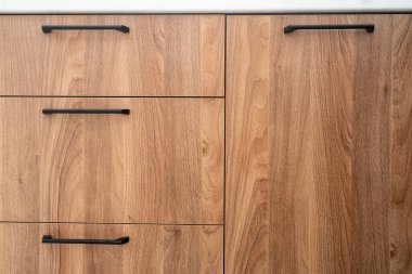 Çağdaş bir mutfakta minimalist siyah saplı pürüzsüz ahşap dolap. Kapalı kapıları, çekmeceleri ve doğal meşesi olan ahşap mobilyalar oturma odasında ön cephede. Evdeki dolabın önü.