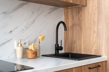 Mermer mutfak köşesinde siyah lavabo, musluk, ahşap dolaplar ve beyaz arka planda bulaşık yıkama aletleri var. Düzenli ev kavramları