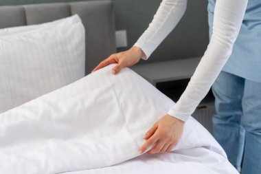 Kadının yakın görüntüsü, otel odasındaki yatağı yapmak, yatağın fotokopisini çekmek. Hizmetçi, elinde yeni bir yorgan olan beyaz bir battaniye tutuyor. Oda servisi, çamaşır günü konseptleri.