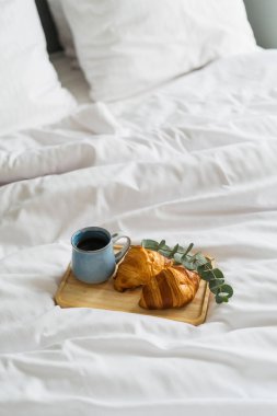 Yatak ve kahvaltı kavramı. Tahta tepsi, bir fincan siyah aromalı kahve ve kruvasan. Lüks oteldeki oda servisi. Evde sakin bir hafta sonu sabahı.