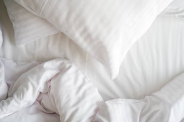 Pörsümüş battaniyeli, beyaz çarşaflı ve hipoalerjenik yastıklı, otel odasındaki temiz çarşafların üzerinde düzleştirilmemiş yatak. Çamaşır günü, evde sabah, rahat uyku konseptleri.