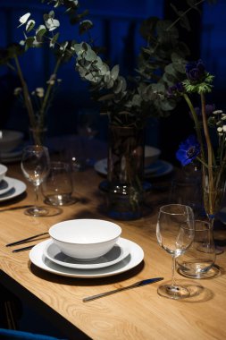 Restoranda romantik bir akşam ya da evde aile toplantısı. Beyaz tabaklar, gümüş eşyalar ve şarap kadehleriyle dolu bir yemek masası çiçekli vazoların yanında duruyor..