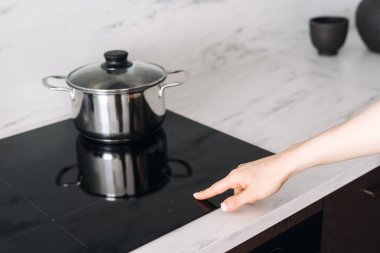 Kadın, indüksiyon ocağındaki dijital ekranda başlat düğmesine basıyor. Kadın evde yemek pişiriyor, modern ev aletlerini kullanıyor. Mutfak aletleri, mutfak konseptleri. Tepesinde tava olan elektrikli soba.