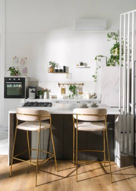 Şık bir evde yemek masasının yanında altın bar tabureleri olan modern bir mutfak sergileniyor. Mermer tezgah, bitkiler, çatal bıçak ve ev dekoru, dikey çekim.