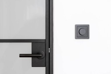 Cam kapının ön tarafında parlak siyah bir kapı kolu var. Yanında da regülatör düğmesi olan, duvara monte edilmiş bir lamba anahtarı var. Minimalist estetiğe sahip çağdaş iç mekanlar için tasarlanmış elementler