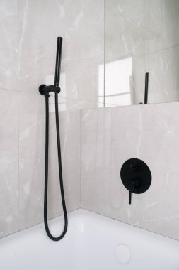 Çağdaş bir banyoda minimalist siyah bir duş başlığı ve musluk bulunur. Zarif kiremitler ve modern apartman ya da otel odasında temiz bir tasarım.