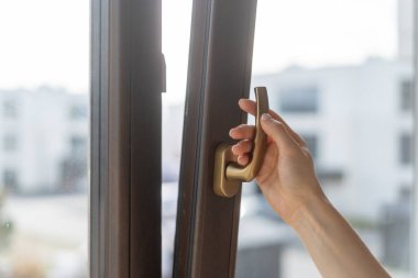 Eller havalandırma için modern bir pencere açmak için uzanıyor. Şehir manzarası ve bina manzarası, camdan görülebiliyor. Yatak odası ya da oturma odası. Plastik balkon kapısında PVC çerçevesi var.