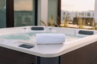 Küvetin kenarındaki beyaz havlular çatı terası seçici odak noktasındaki bahçe bahçesine karşı. Lüks oteldeki açık havuz. Çatıda küveti olan Wellness Resort çatı katı dairesi.