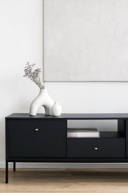 Şık bir siyah dolap, arka planda hafif bir vazo ile süslenir. Oturma odasındaki klozette ev dekoru ve maket resim. Konforlu evdeki resim çerçevesini dikey çekimde kopyala