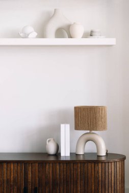 Tahta büfe, minimalist okuma lambası, kitaplar ve tarafsız oturma odasındaki duvara karşı dekoratif seramik vazo ile dikey çekim.