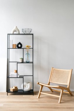 Süslü siyah kitaplık dekoratif vazolar, kitaplar ve saksı bitkileriyle dolu. Ev dekoruyla rafa yakın, parlak, havadar bir yaşam alanında tahta şezlong, dikey çekim.