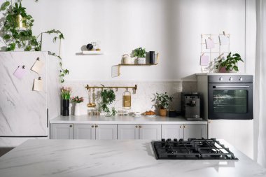 Çağdaş dairede modern iç tasarım. Pürüzsüz bir mutfak, gaz sobasının tepesinde mermer bir tezgâha sahiptir. Ev bitkileri ve modern aletlerle bulanık arka plana karşı yemek masası