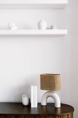 Süslü bir okuma lambası, içinde dekoratif eşyalar olan koyu ahşap bir masanın üzerinde kitaplara yakın durur. Oturma odası. Raflarda ev dekorasyonu var. Klozetin üstünde, rahat dairede.