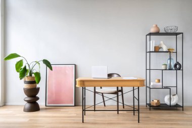 Oda, şık dekoratif elementler ve iç mekan bitkileriyle çevrili, sakin bir çalışma atmosferini teşvik eden, bir sandalyeyle eşleştirilmiş basit bir ahşap masaya sahip..