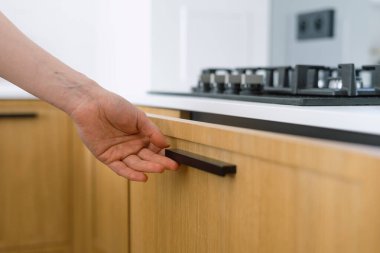 Modern bir mutfakta bir el ahşap çekmeceyi açıyor ya da kapıyor, yakın çekim. Beyaz tezgahlı modern mobilyalar. Dolapların üzerine gaz sobası ve bulaşık malzemeleri için depolama kutusu.