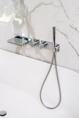 Seramik küvetin üzerine beyaz mermer bir duvara el yapımı duş hortumuyla dikey krom musluk yerleştirilir. İç mekan elementi modern uzayda çağdaş bir görünüm yaratıyor, yakın çekim