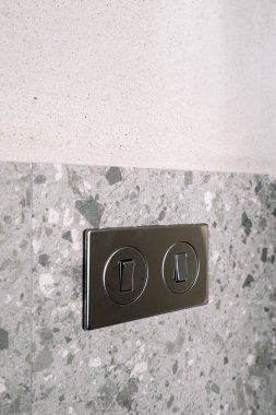 Gri taş ve betondan oluşan bir duvarın üzerindeki metal çerçevedeki şık ışık anahtarının yakın görüntüsü, modern tasarım elementlerini iç dekorda, dikey çekimde sergiliyor.