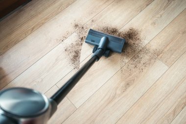 Elektrikli süpürge, açık renkli ahşap zeminlerden toprak ve döküntü toplayarak kapalı alanda düzenli bir çevre oluşturma sürecinde.