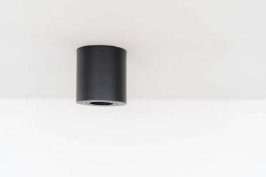 Küçük enerji tasarruflu lamba armatürüne sahip siyah silindirik tavan lambası oturma odasındaki fotokopi duvarında asılı duruyor. Modern dairede spot ışığı. Enerji tasarruflu teknolojiyle iç içe