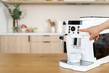 Otomatik espresso makinesindeki kadın el ile başlatma düğmesine basarak evde sabah kahvesi yap, kırpılmış atış. Mutfak masasının üzerinde kapsüllü kahve makinesi var.