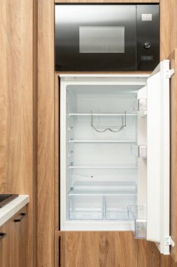 Mikrodalga fırın ve boş buzdolabı ahşap mutfak dolabında. Dairesinde açık kapısı olan modern dondurucunun ön görüntüsü. Minimalist iç tasarım, dikey çekim.